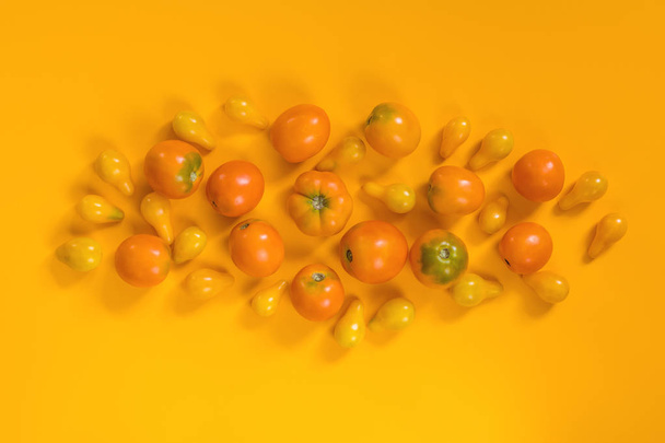 Many different orange yellow tomatoes on yellow surface.  Beautiful food art background, top view. - Foto, afbeelding