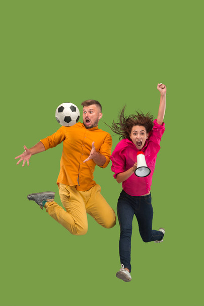 Forward to the victory.The young couple as soccer football player jumping and kicking the ball at studio on a green - Foto, immagini