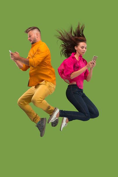 Full length of young couple with mobile phone while jumping - Фото, зображення