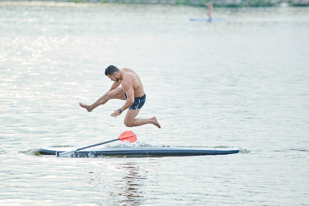 Sportman springen van sup board in water van de meren. - Foto, afbeelding