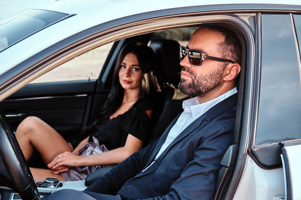 Beautiful well-dressed couple sitting on the front seats in the luxury car. - Фото, зображення
