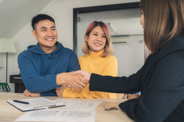 Happy young Asian couple and realtor agent. Cheerful young man signing some documents and handshaking with broker while sitting at desk. Signing good condition contract. - Photo, Image