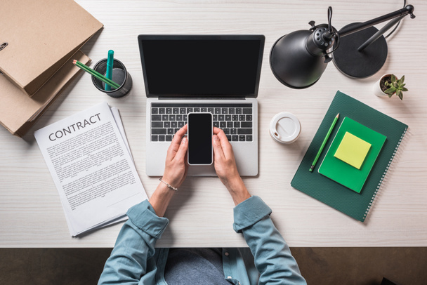 обрезанный образ бизнесмена, использующего смартфон за столом с ноутбуком, контрактом и одноразовой чашкой кофе
  - Фото, изображение