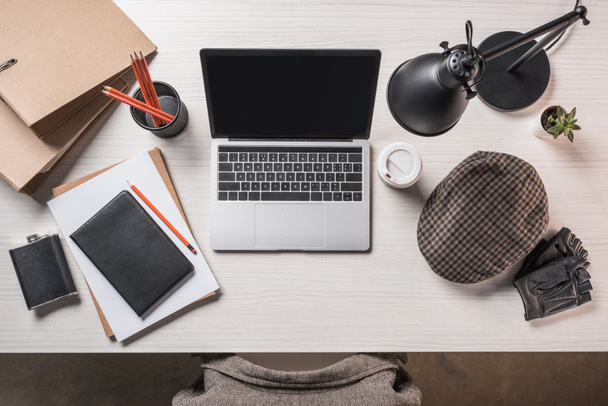 повышенный вид на рабочее место с флягой, кофе, кепкой, канцелярскими принадлежностями и ноутбуком на столе
  - Фото, изображение