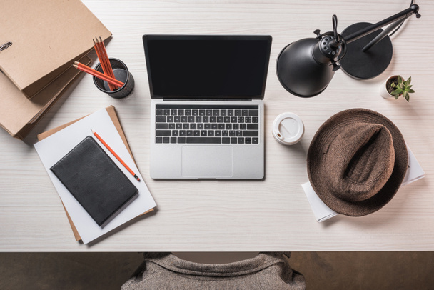 top view of laptop with blank screen, fedora hat, coffee cup and stationery on table  - Photo, Image