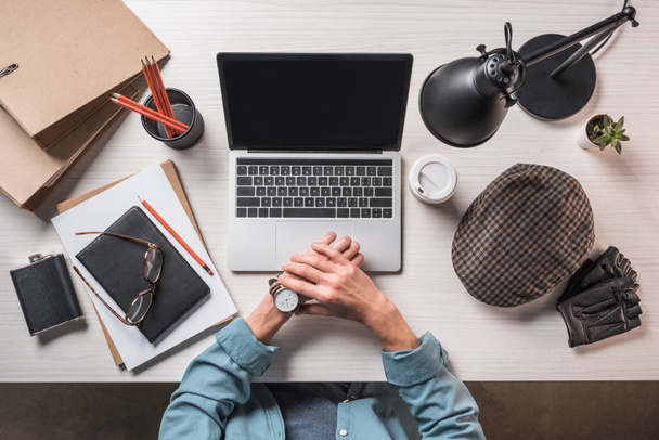 обрезанный образ стильного бизнесмена, проверяющего наручные часы за столом с ноутбуком и канцелярскими принадлежностями
  - Фото, изображение