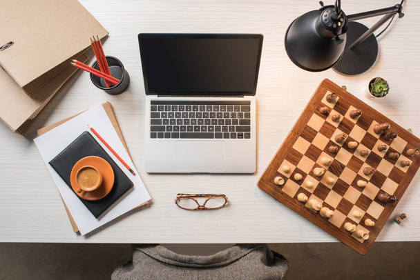 elevated view of workplace with eyeglasses, coffee cup, chessboard and laptop on table - Φωτογραφία, εικόνα