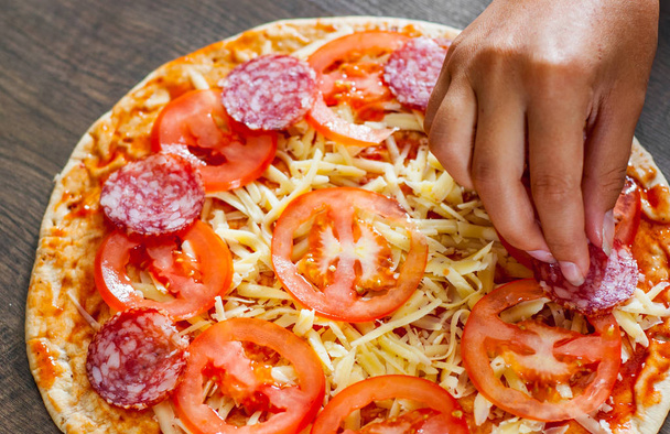 Приготування піци. Рука Кука Жінка одягає тісто скибочка салямі. прийняття італійська піца з дерев'яними тлі - Фото, зображення