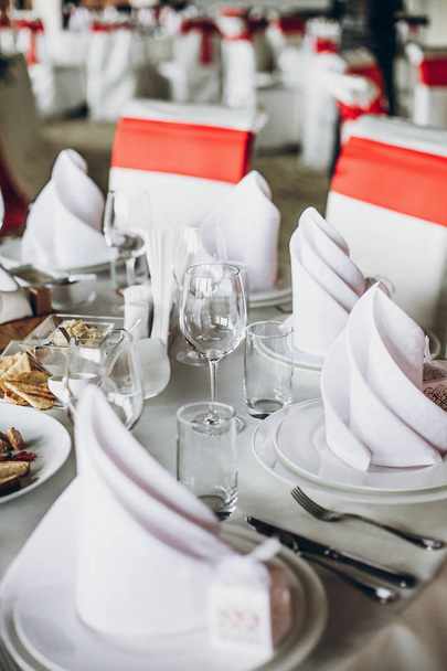 елегантний весільний стіл з їжею, срібні столові прибори, порожні окуляри. налаштування з червоною прикрасою, білими шовковими стільцями та серветками. розкішне харчування в ресторані на весілля
 - Фото, зображення
