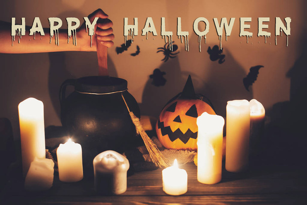 Happy Halloween text concept. Spooky Halloween sign. Witch hand boiling potion spell in cauldron, Jack o lantern, pumpkin,candles, broom and bats, ghosts in night - Foto, afbeelding