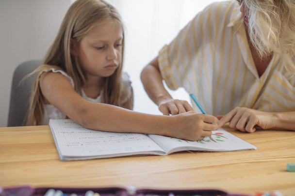 Cute blonde Caucasian girl studying at home with her mother helping. - Photo, image