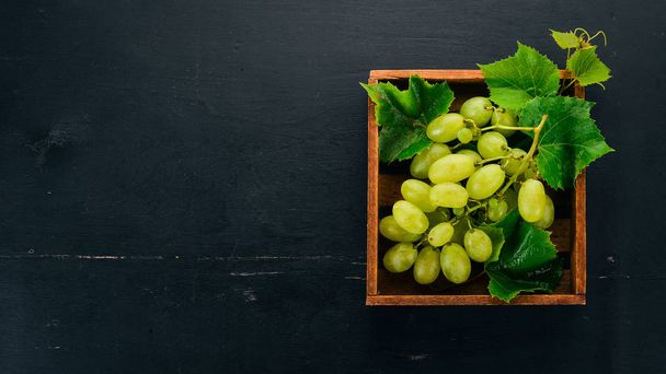 Grapes in a wooden box. Leaves of grapes. Top view. On a black background. Free space for text. - Φωτογραφία, εικόνα
