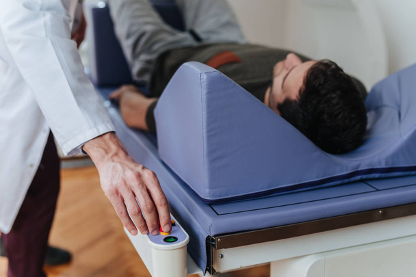 Mão de um técnico médico operando o densitômetro de osso enquanto seu paciente está deitado na cama
. - Foto, Imagem