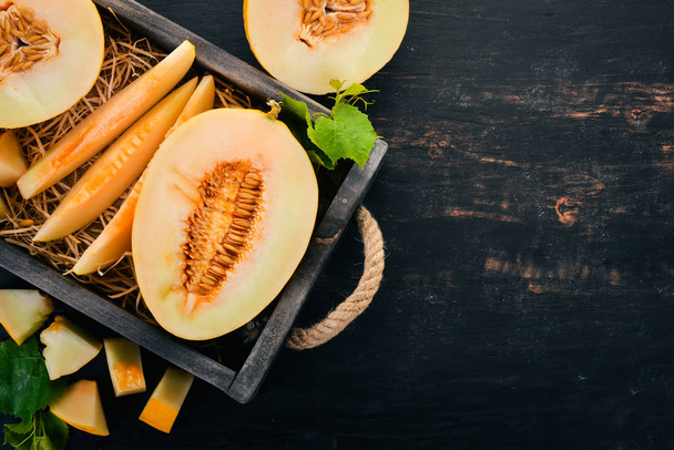 Melon in a wooden box. Sliced to pieces of melon. On a wooden background. Free space for text. Top view. - Φωτογραφία, εικόνα