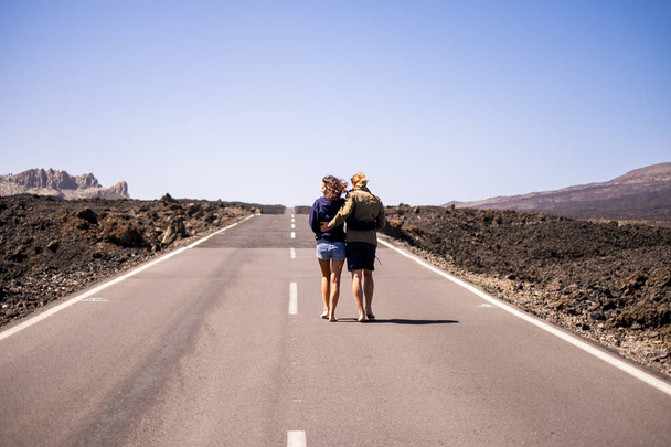 rear view of nice young couple hugging and walking on long way road  - Photo, Image