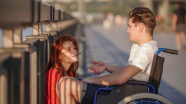 Guy en fauteuil roulant dit quelque chose à la fille aux cheveux roux et elle Iistens soigneusement, sur la promenade en soirée d'été
 - Photo, image