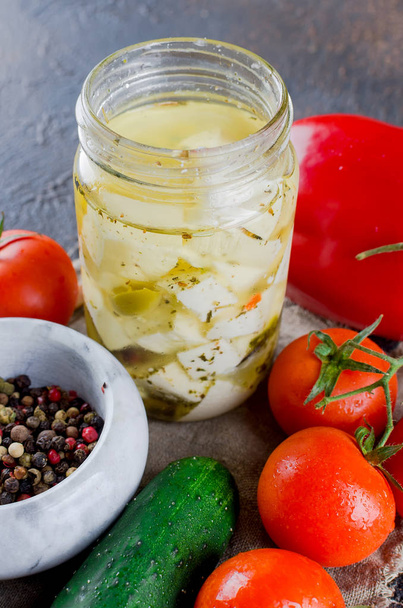 Marinated spicy  feta in a jar, tomatoes and cucumbers for salad. On a dark background. Copy space for your text.  - Zdjęcie, obraz
