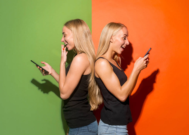 Portrait of a happy smiling casual girls with mobile phones over studio background - Φωτογραφία, εικόνα