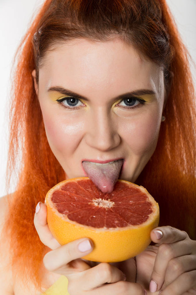Young redhead woman licks a grapefruit on a white background. concept of healthy eating - Photo, Image