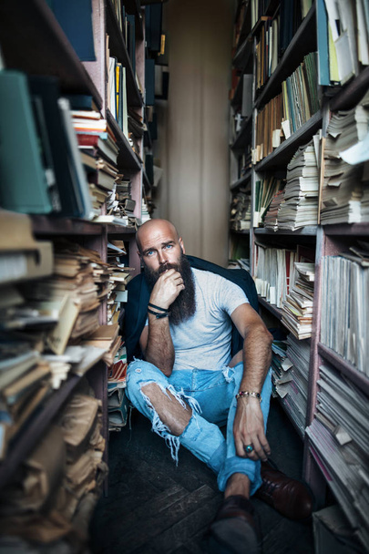 Upset hipster man sitting on floor in library. Depression concept - Photo, image