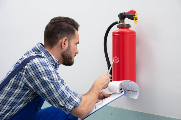 Close-up Of A Young Male Technician Checking Fire Extinguisher Writing On Document - Fotografie, Obrázek