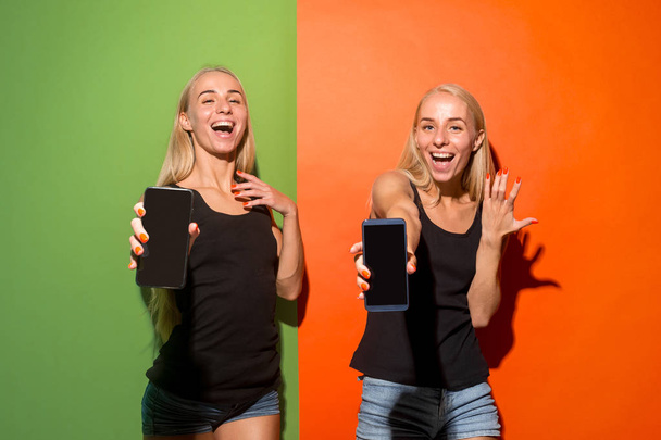 Portrait of a confident casual girls showing blank screen mobile phone isolated over studio background. - Fotoğraf, Görsel