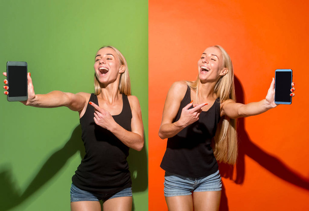 Portrait of a confident casual girls showing blank screen mobile phone isolated over colorful background - Fotoğraf, Görsel