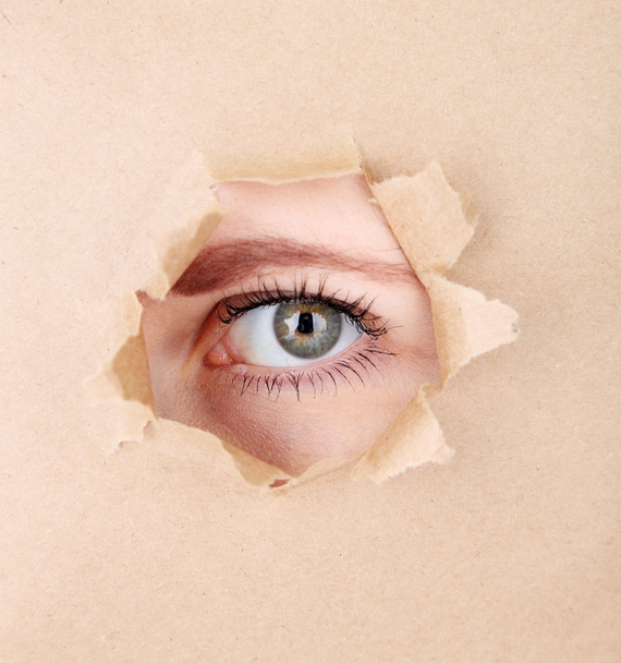 Female eye looking through hole in sheet of paper - Фото, изображение