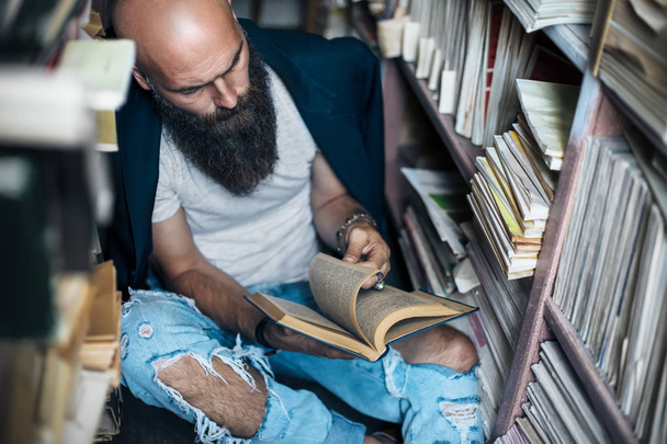 Stylish hipster man reading book sitting on floor in bookstore. Education, hobby concept - Foto, imagen