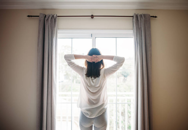 Ganzkörperporträt einer Frau, die sich nach dem Aufwachen am Fenster ausstreckt. Guten Morgen  - Foto, Bild