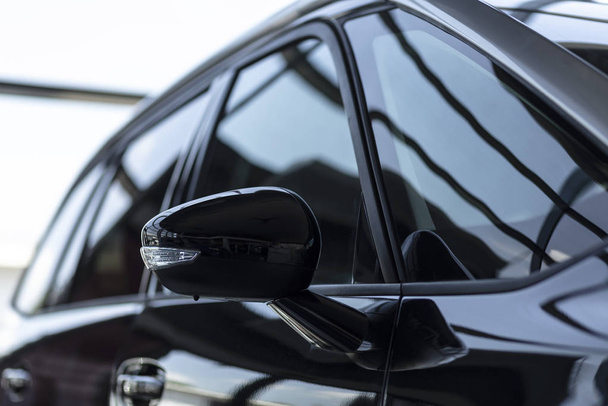 Close-up of a side mirror of a black family car for sale at a modern dealership - Foto, immagini