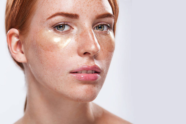 Beautiful model woman with ginger hair and frackles and closeup gold patches for skin care - Foto, immagini