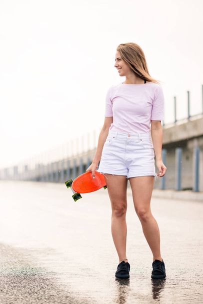 Young Beautiful Blonde Girl with Bright Skateboard on the Bridge - Fotografie, Obrázek