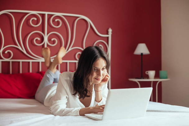 Happy woman working on laptop relaxing on bed at home.  - Foto, imagen