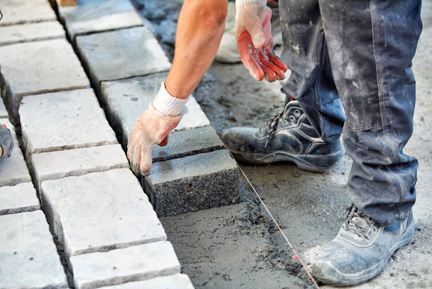 Las manos con guantes de un trabajador usan un martillo para colocar adoquines de piedra. Trabajador creando pavimento utilizando bloques de adoquines y piedras de granito
. - Foto, Imagen