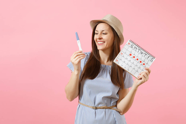 Mulher feliz excitada em vestido azul, chapéu segurar na mão teste de gravidez, calendário de períodos para verificar dias de menstruação isolado em fundo rosa. Médico, saúde, conceito ginecológico. Espaço de cópia
 - Foto, Imagem