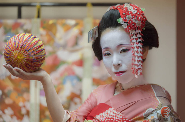 Ładna dziewczyna japoński gejsza w kimono posiadający piłkę temari w ręku. - Zdjęcie, obraz