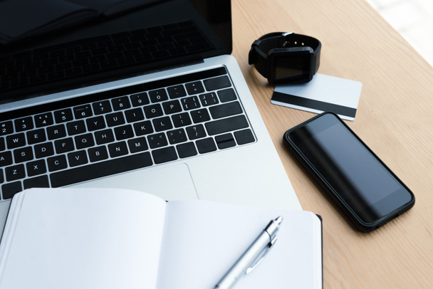 vista ad angolo alto di laptop, smartwatch, smartphone, carta di credito e notebook in bianco con penna sul tavolo
 - Foto, immagini