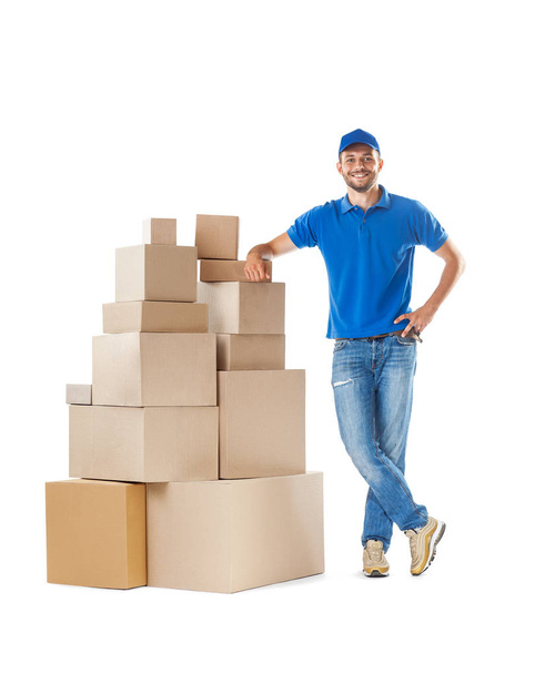 Full length portrait of delivery man standing near stack of boxes isolated on white background - Fotografie, Obrázek