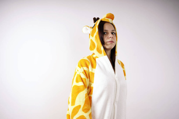 girl in a bright children's pajamas in the form of a giraffe. emotional portrait of a student. costume presentation of children's animator. Slippers in the form of cat's paws.          - Foto, afbeelding
