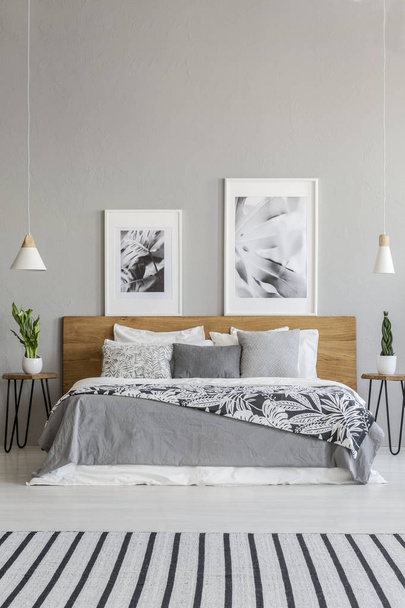 Posters on wooden headboard of bed with patterned blanket in grey bedroom interior with carpet. Real photo - Fotografie, Obrázek