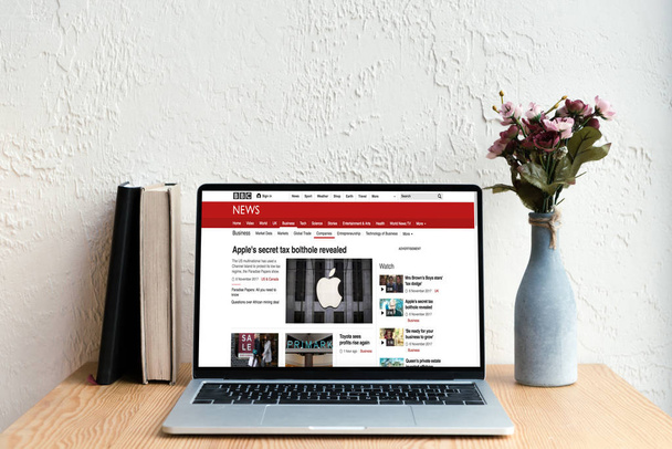 laptop with bbc news website on screen, books and flowers in vase on wooden table - Fotoğraf, Görsel