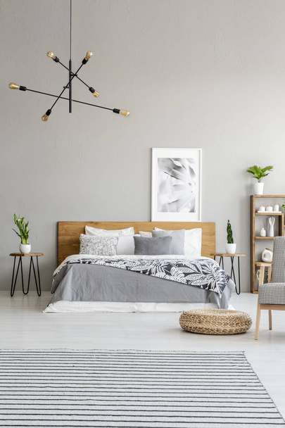 Gedessineerde tapijt en poef in ruime grijs slaapkamer interieur met poster boven houten bed. Echte foto - Foto, afbeelding