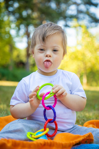 Retrato de lindo niño pequeño con síndrome de Down jugando en la manta en el día de verano en la naturaleza
 - Foto, imagen