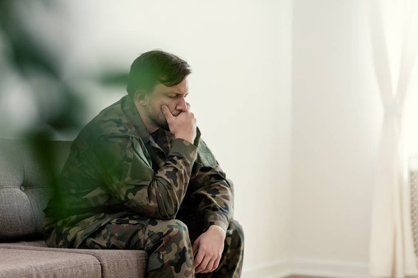 Sad soldier in uniform covering his mouth while sitting on a sofa - Fotografie, Obrázek