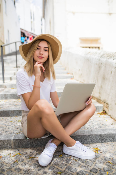 Young woman with laptop sitting on stairs outdoors - Foto, imagen