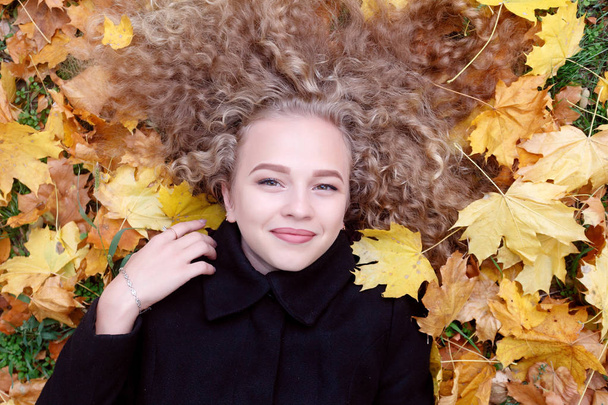 Beautiful young woman with curly hair, green eyes. girl in casual clothes relaxing in park in good autumn weather, covered with fallen leaves. - Foto, afbeelding