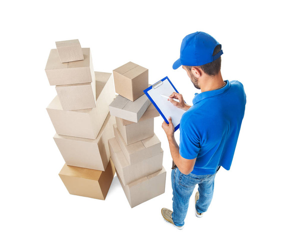 Vista superior del repartidor tomando notas cerca de la pila de cajas de paquetes aisladas sobre fondo blanco
 - Foto, Imagen