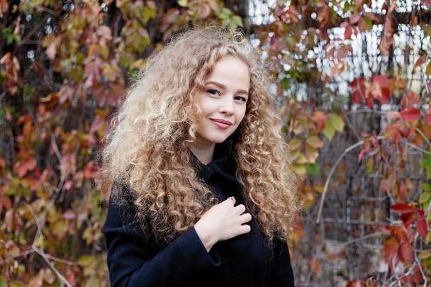 Beautiful young woman with curly hair, green eyes. girl in casual clothes relaxing in park in good autumn weather, covered with fallen leaves. - Zdjęcie, obraz