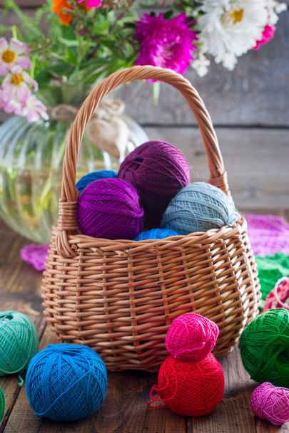 Multi-colored balls of cotton thread for crocheting in a wicker basket on a wooden table, selective focus - Foto, afbeelding